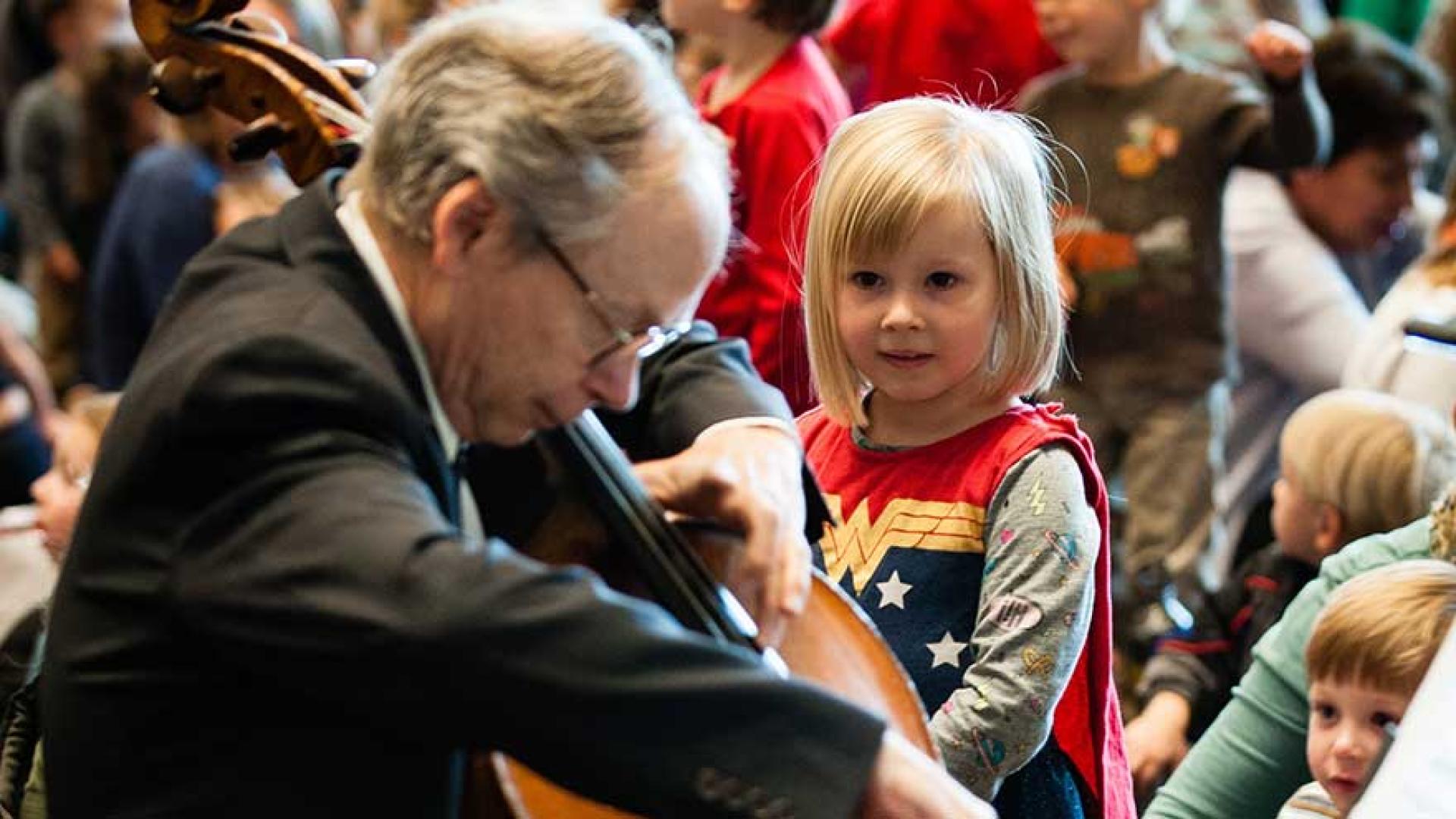 Young girl watching old man playing the cello.