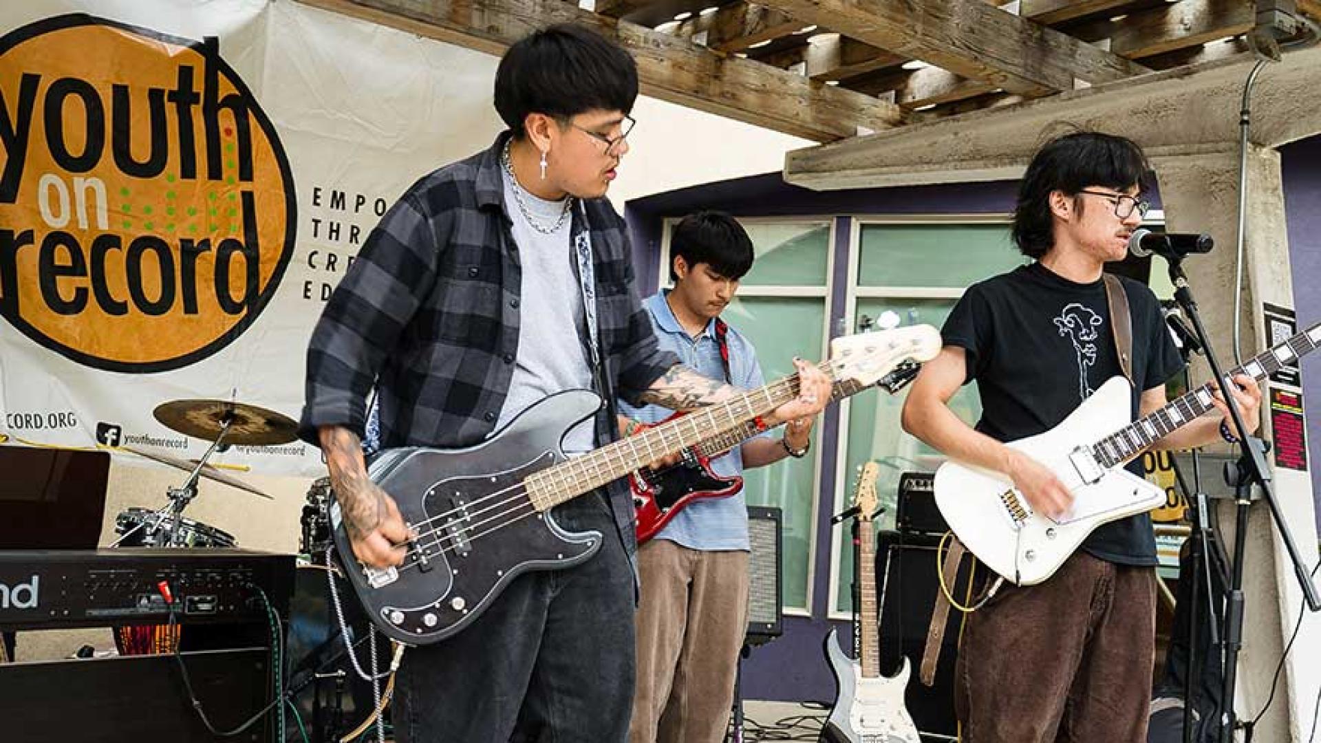 Three teens playing electric guitars on stage.